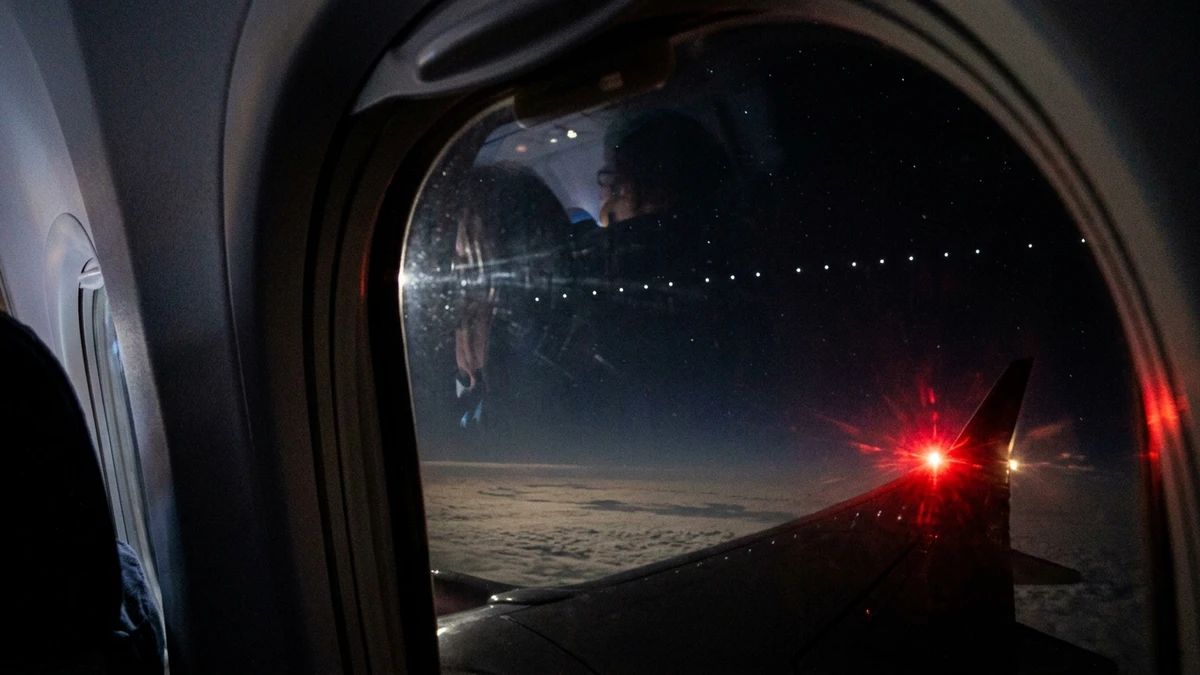 A line of evenly spaced white lights photographed at night through an airliner cabin window above cloud