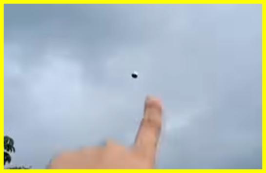 Video still from Buga, Colombia showing a witness pointing at a small dark spherical object hovering in the overcast sky, March 2025
