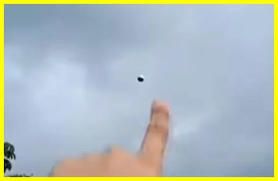Video still from Buga, Colombia showing a witness pointing at a small dark spherical object hovering in the overcast sky, March 2025