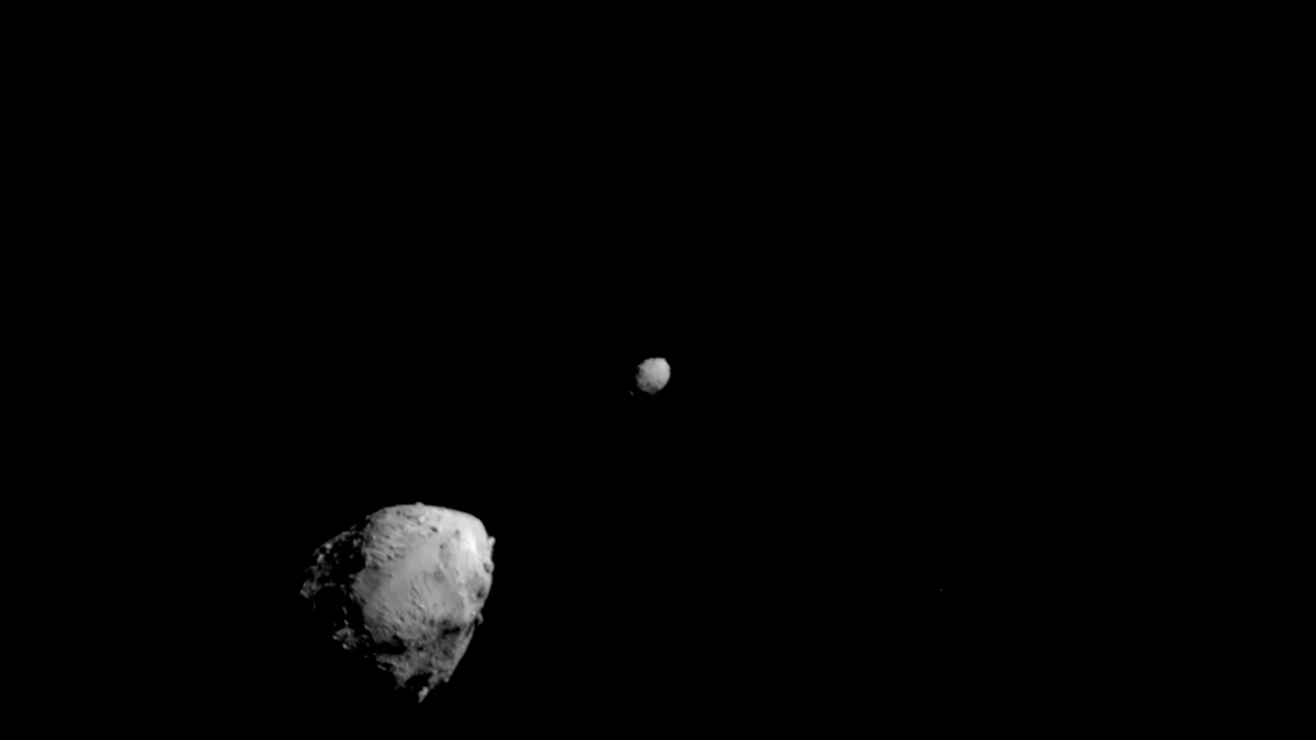 Black and white photo of the large lumpy asteroid Didymos in the lower left and the smaller round asteroid Dimorphos near the centre, taken by DART shortly before impact