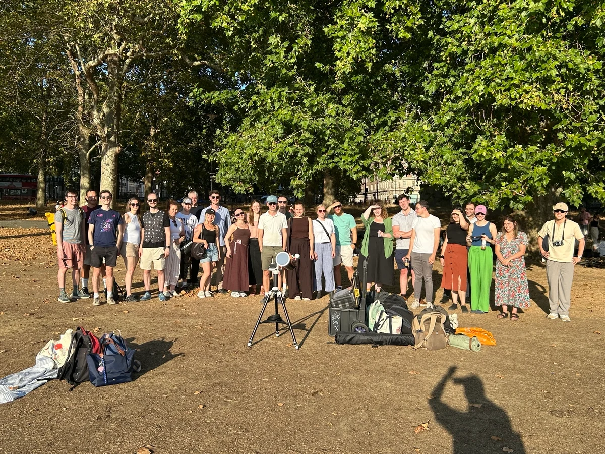 Adult members of the SPARTA Astronomy Society standing behind a small telescope and observing equipment in Hyde Park during the 2026 solar eclipse