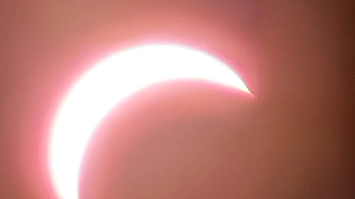 Bright crescent sun glowing through thin cloud during the 2026 partial solar eclipse, photographed on a phone from Dunstable Downs
