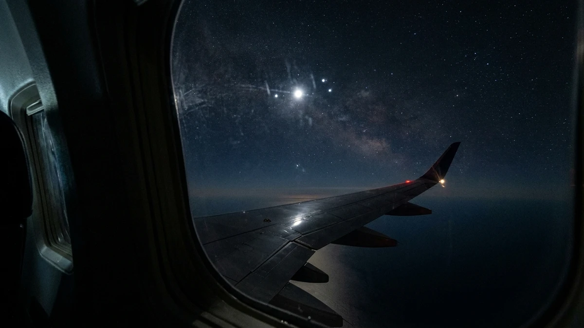 View from an airliner window at night showing faint bright lights high above the aircraft over the Atlantic