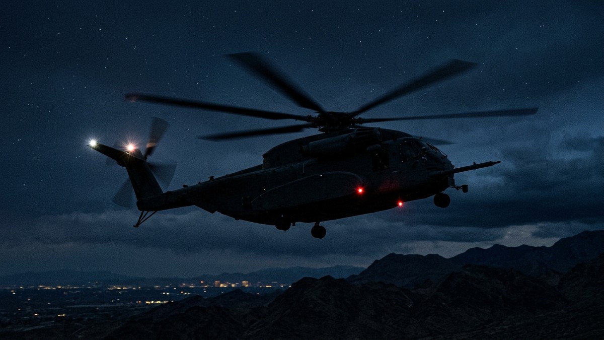 An intelligence helicopter silhouetted against a dark sky at night, viewed from a slightly elevated angle