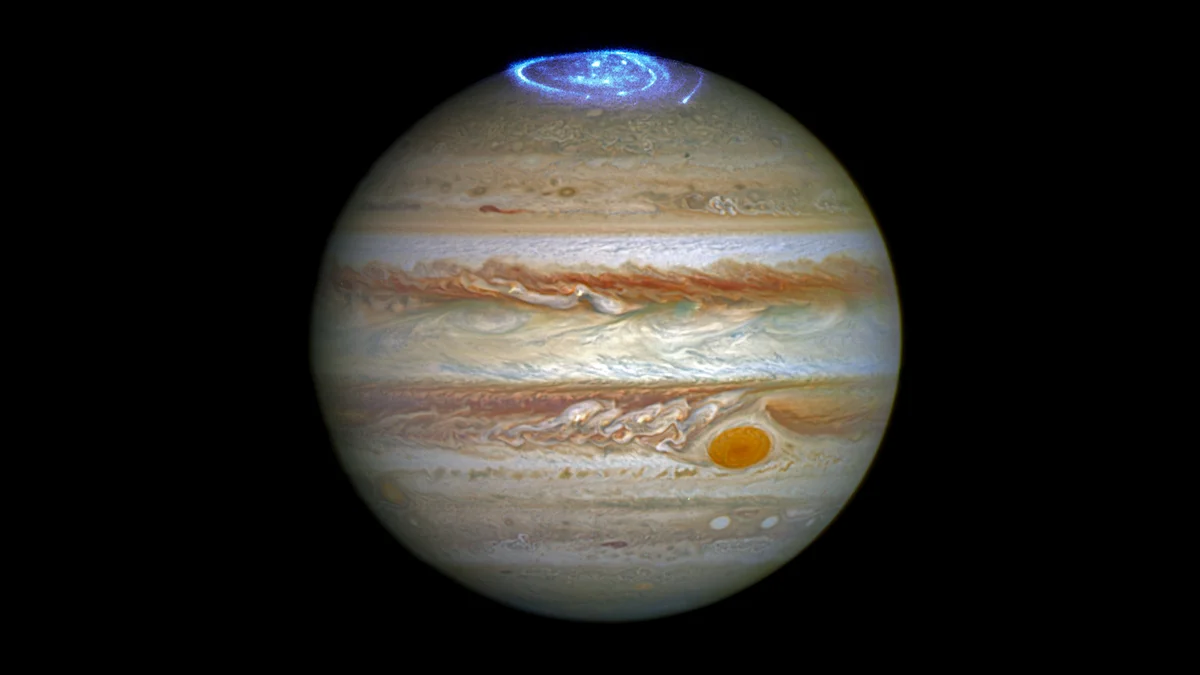 Hubble image of Jupiter showing its cloud belts and Great Red Spot, with a bright blue ring of auroral light glowing around the north pole