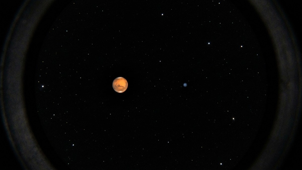 Simulated telescope view showing Mars as a small orange disc next to a tiny blue dot representing Neptune