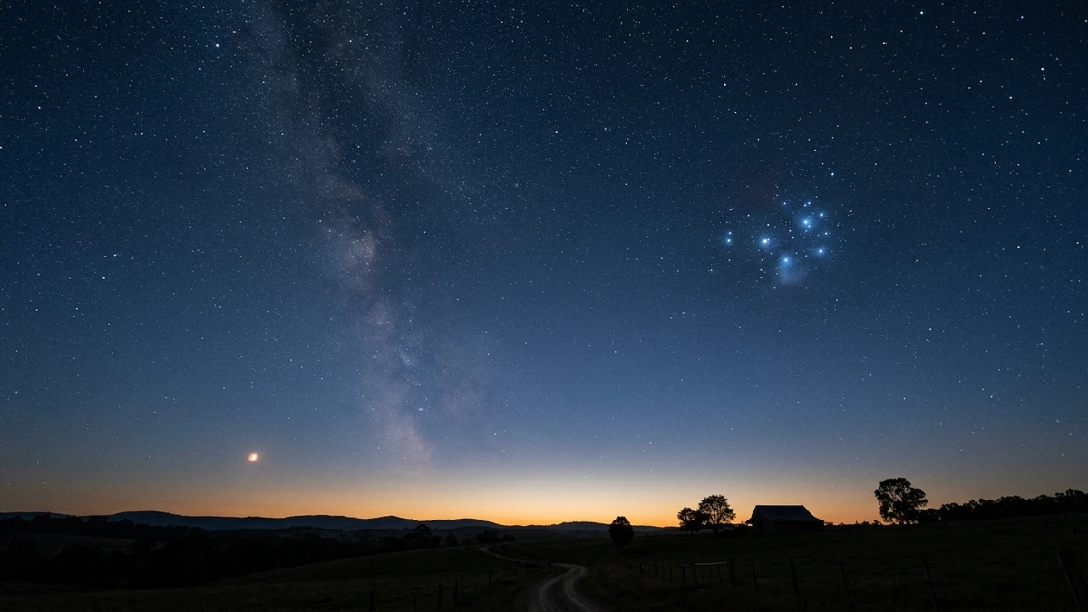 Wide view of orange Mars to the lower left of the blue Pleiades cluster, low in a pre-dawn sky over a UK horizon