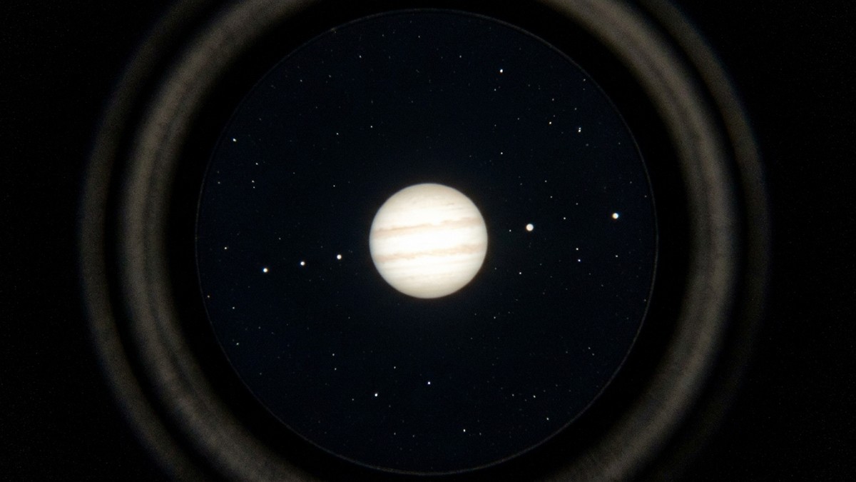 View through binoculars showing Jupiter with its four Galilean moons as tiny dots alongside the bright planet