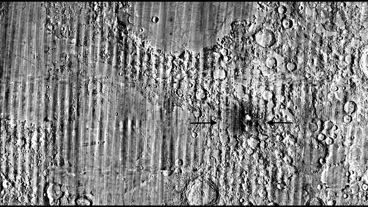 Wide grey change-detection map of the Moon built from Lunar Reconnaissance Orbiter images, with two black arrows pointing to a small bright spot ringed by a dark halo that marks the new McGetchin crater