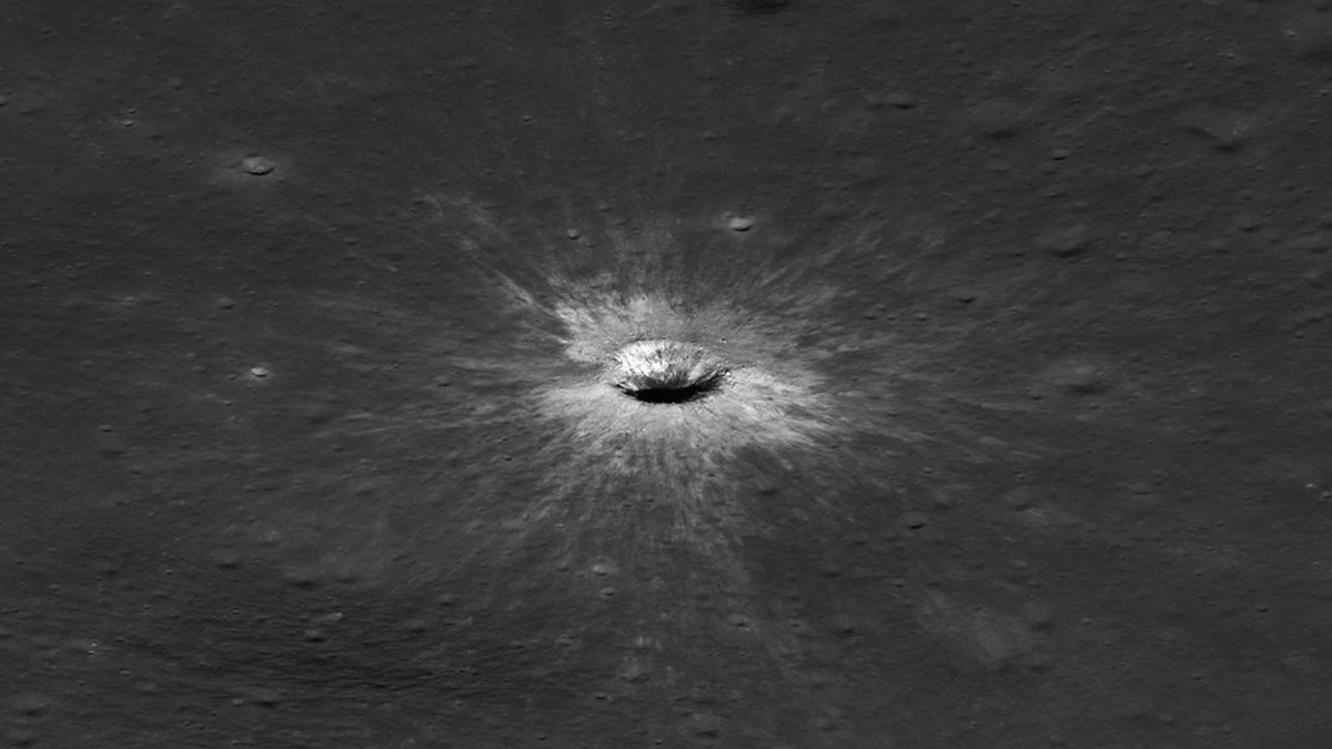 Side-on Lunar Reconnaissance Orbiter view of McGetchin crater, a small oval bowl with a bright raised rim and dark floor, with fine bright streaks radiating across the surrounding grey surface