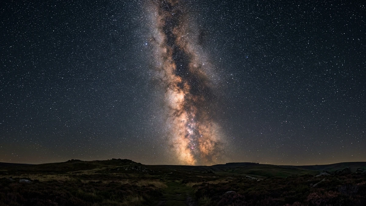 The summer Milky Way arching over a dark British countryside landscape with the Great Rift visible as a dark lane through the star clouds