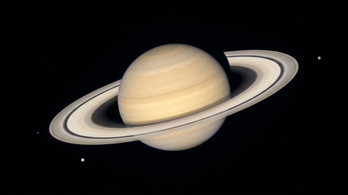 Saturn and its rings as seen through a small telescope, a pale yellow globe surrounded by a bright ring system against a black sky