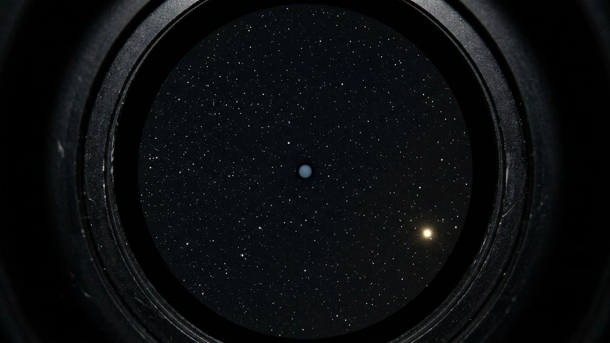 A small telescope view showing Neptune as a tiny blue-grey disc among faint stars, with Saturn bright at the edge of the field