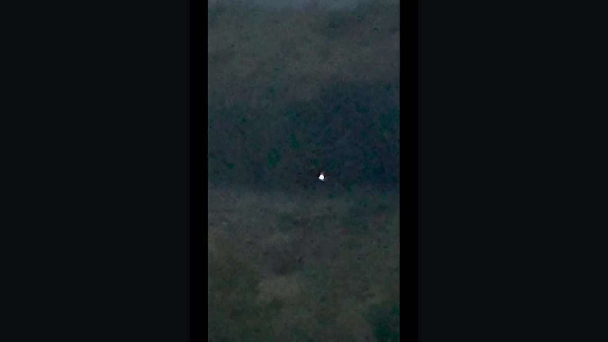 Brightened frame from the FBI-released eyewitness video showing a small white luminous orb hovering over dark water at dusk