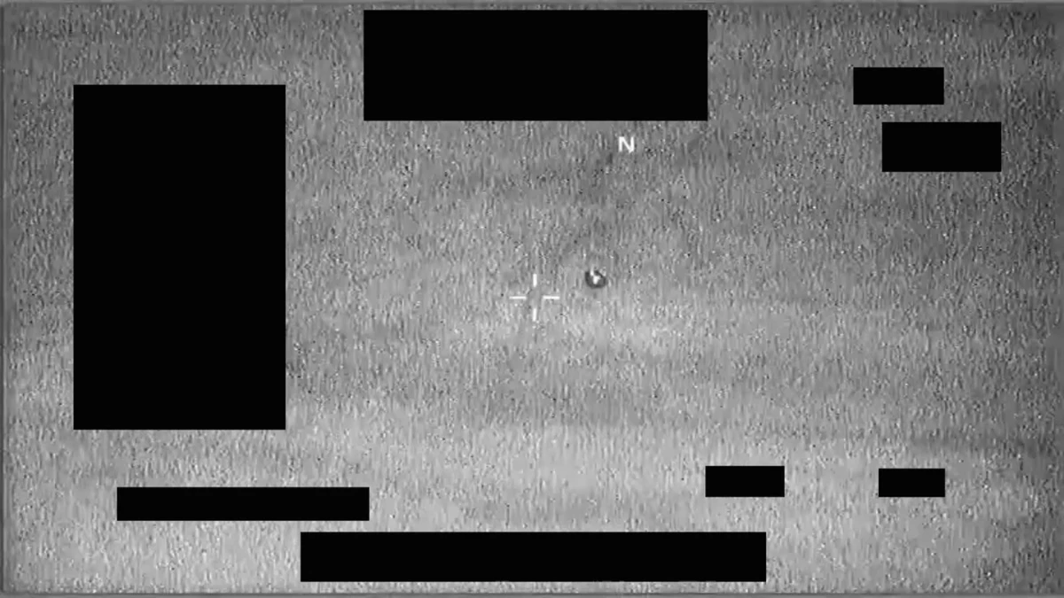 Monochrome infrared frame from DOW-UAP-PR112 showing a small dark object inside a tracking reticle against a grainy pale background, with a north indicator and black redaction boxes around the edges