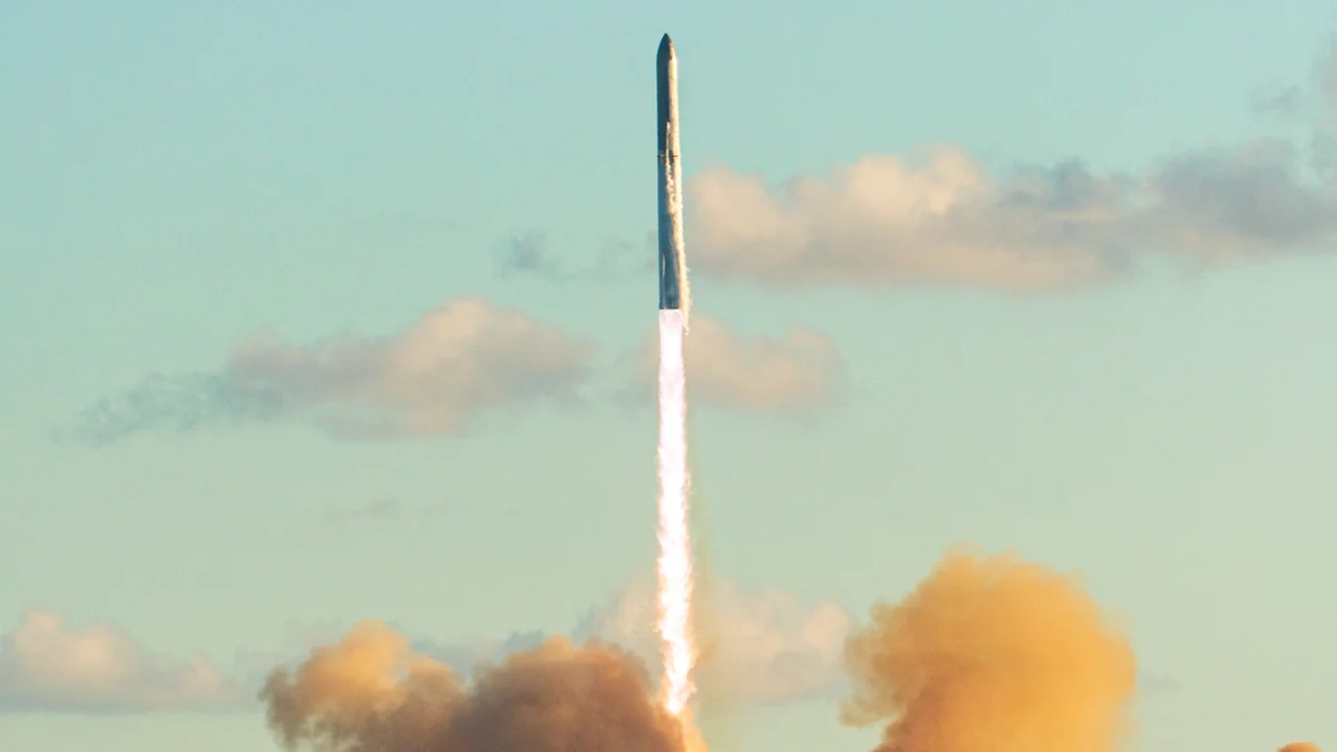 Starship climbing into a pale blue sky on a bright white exhaust trail above billowing orange clouds