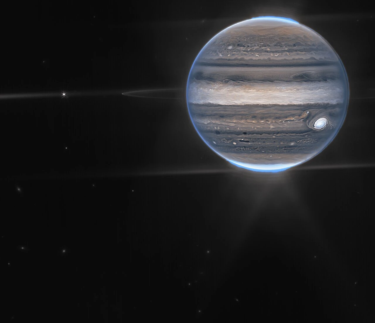 Jupiter photographed by the James Webb Space Telescope showing glowing auroras at both poles, faint ring system and three moons against a black background