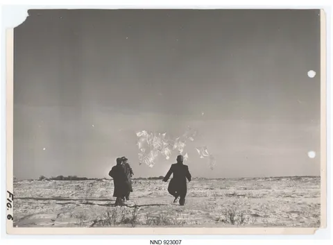 Black-and-white photo of two men launching a cluster of pillow balloons.
