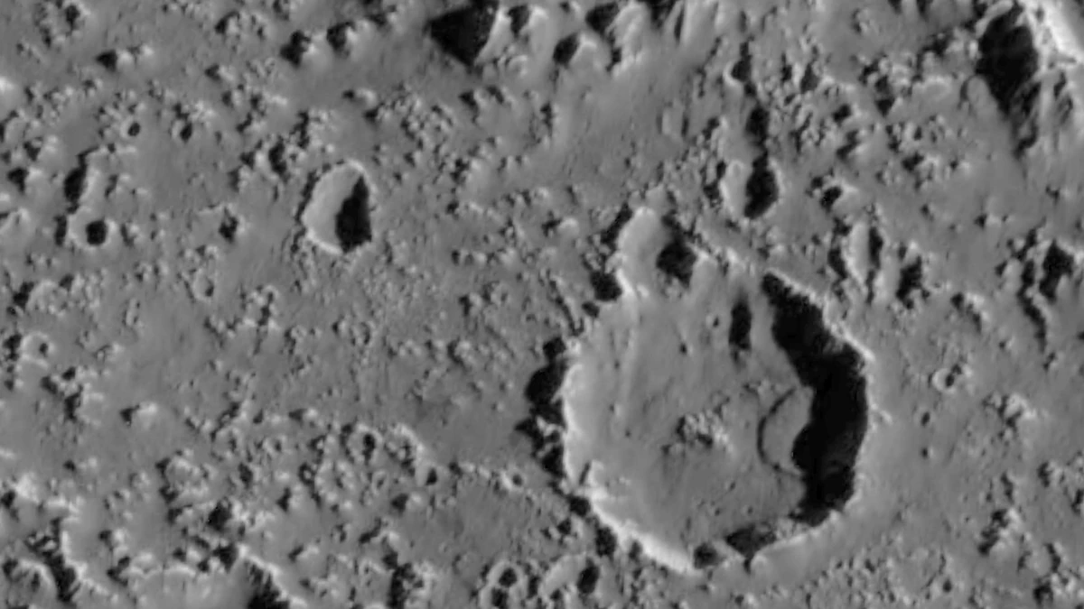 A large crater on Callisto in black and white, with a smooth slumped floor and many smaller craters around it, photographed by Galileo