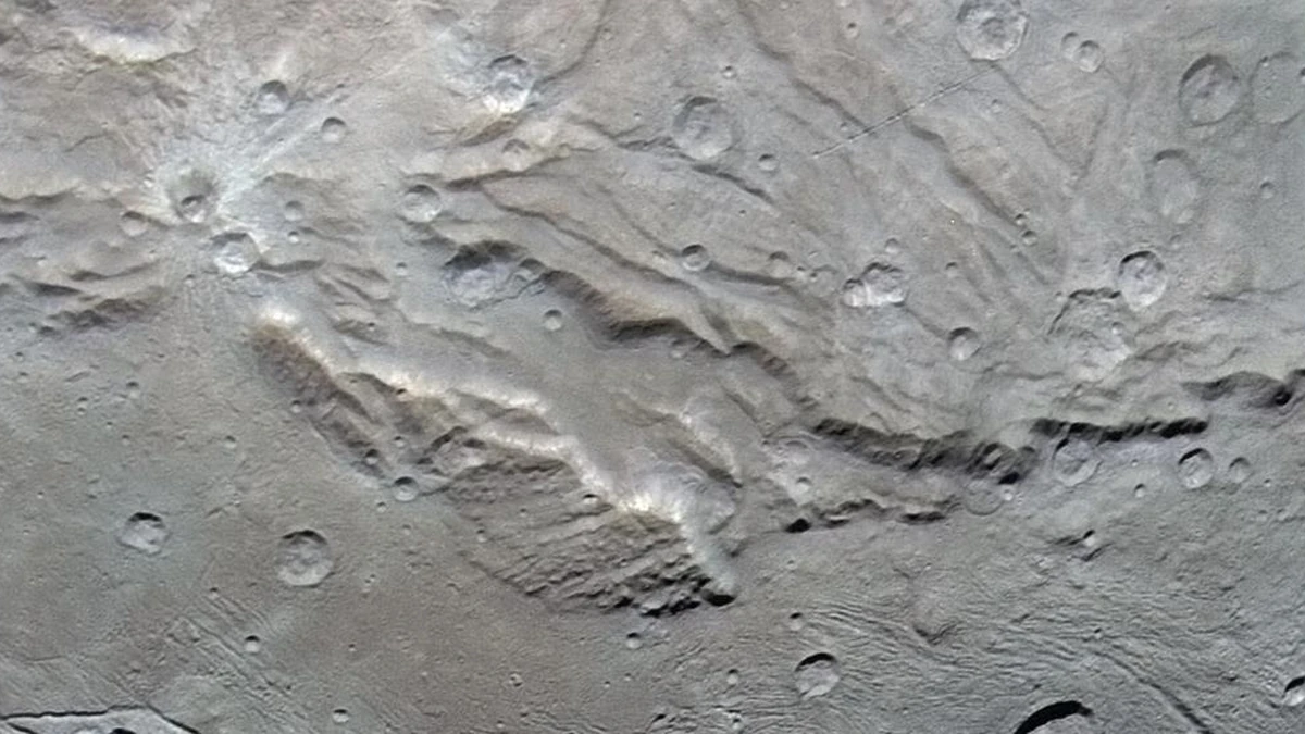 Grey-brown close-up of Charon's surface, with a long steep-walled canyon crossing cratered, rolling plains