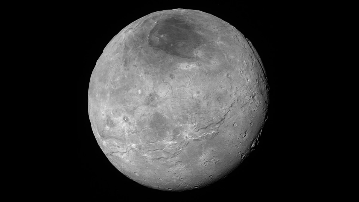 Sharp black-and-white New Horizons view of Charon's whole disc, with a dark patch at the north pole, long cracks across the middle and craters on the right