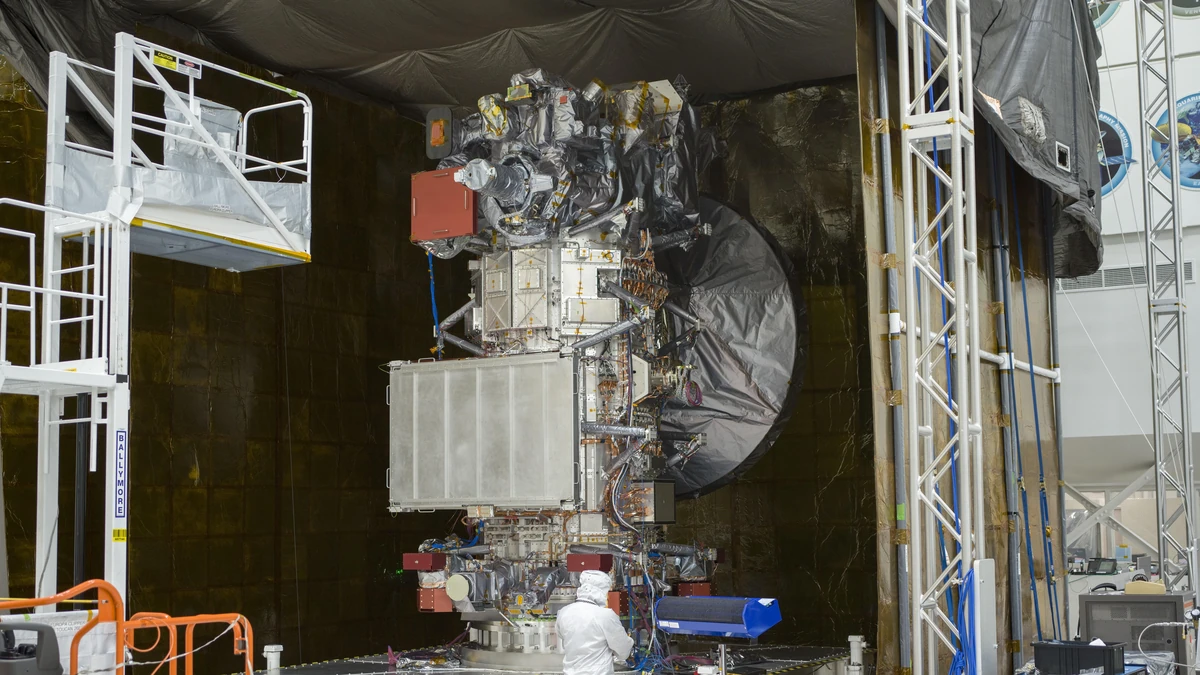 The Europa Clipper spacecraft standing in a clean room at NASA's Jet Propulsion Laboratory, with a technician in white protective clothing at its base and scaffolding on either side