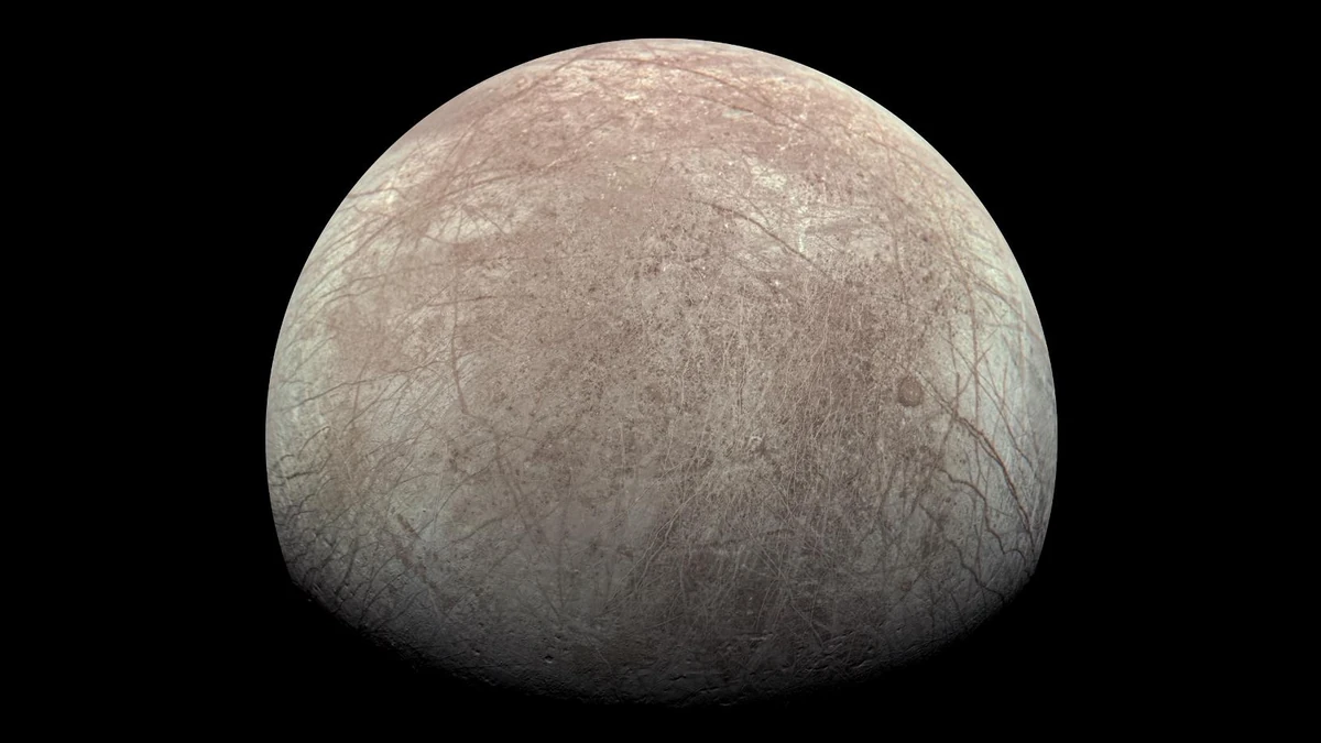 Europa photographed by Juno's JunoCam, a cream and pink-brown globe covered in a web of cracks and ridges, with the lit side facing the camera