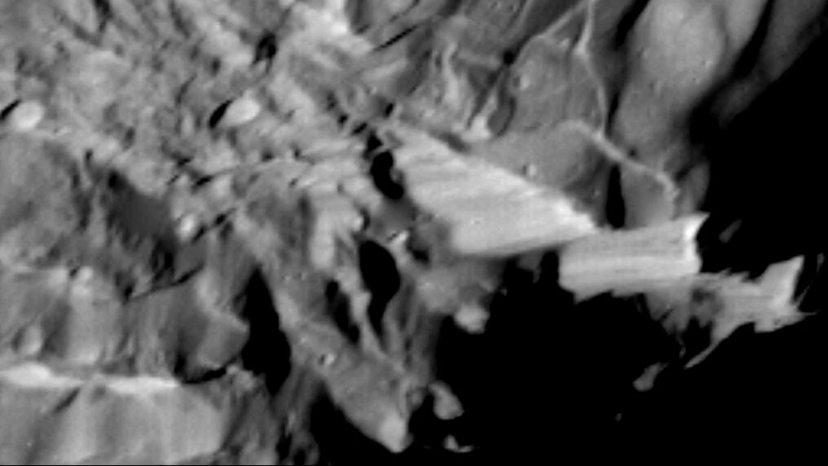 Black-and-white Voyager 2 close-up of Miranda's rugged terrain, with a steep, bright fault scarp at the edge of the disc and black space beyond it on the right