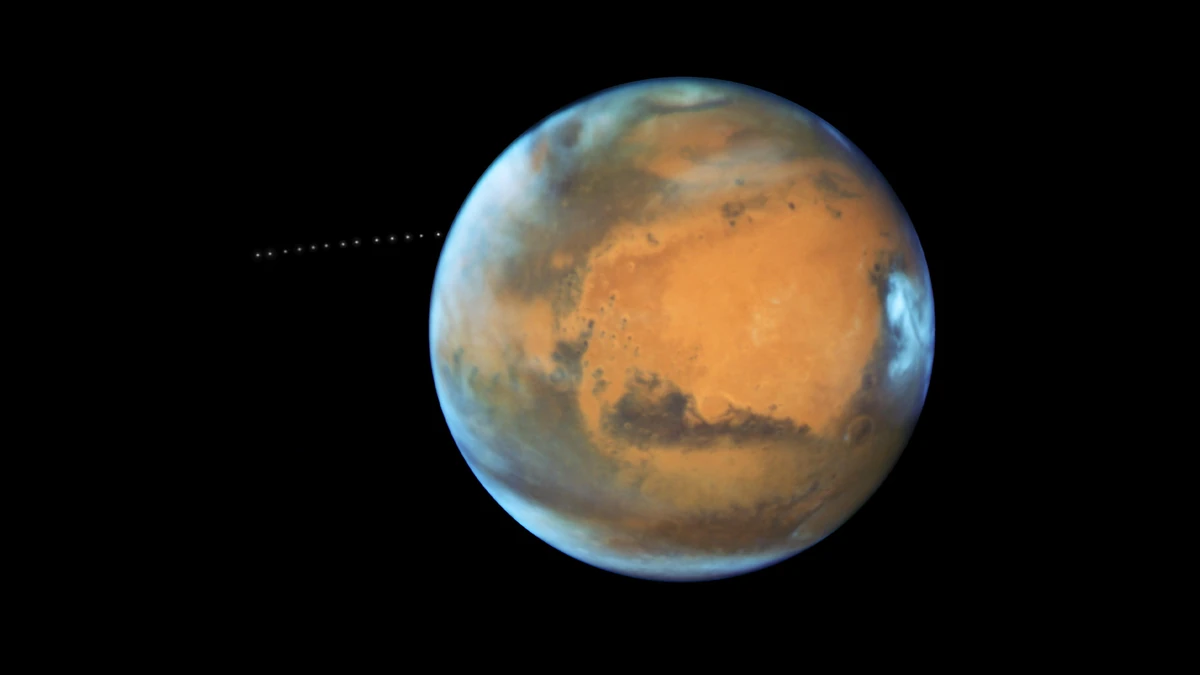 Mars photographed by Hubble with a line of faint dots to the left of the planet marking the path of the tiny moon Phobos over 22 minutes