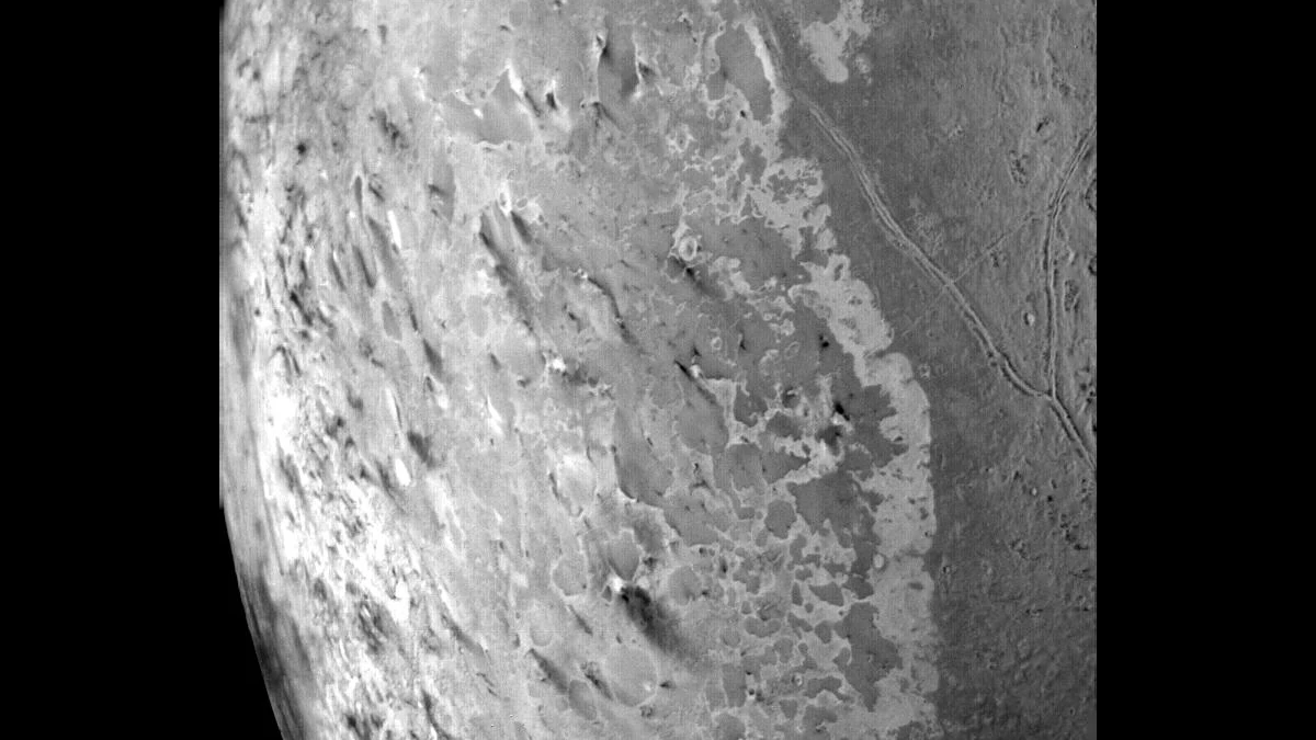 Black-and-white Voyager 2 view of Triton's south polar terrain, with dozens of dark streaks pointing the same way across bright, mottled ice